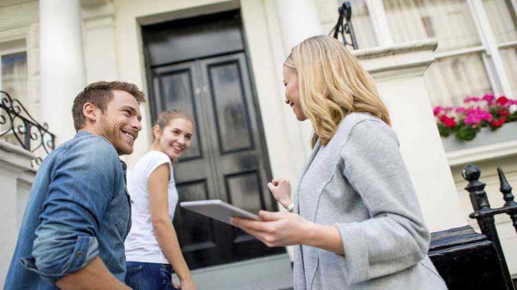Realtor talking to a young couple on a front porch.