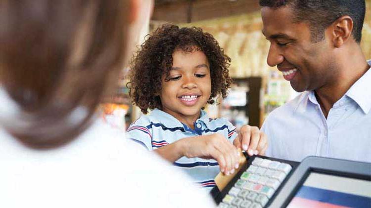 A dad is letting his young son hold his credit card to swipe at a store cash register.