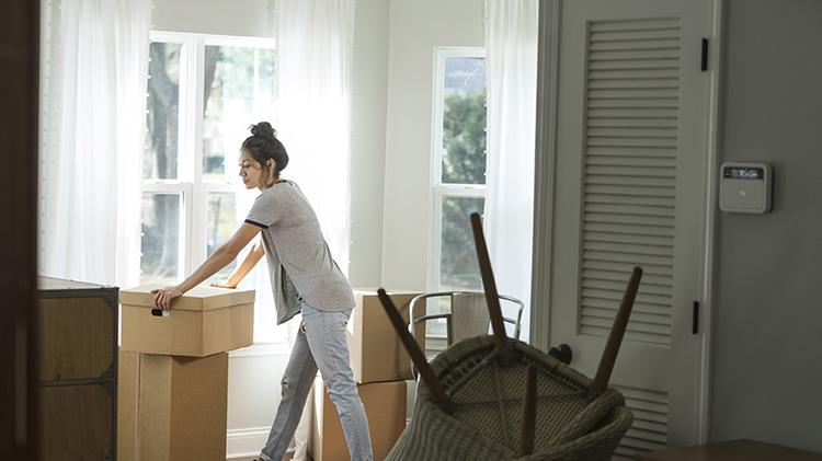 A woman leans against a packing box while packing to move after her divorce