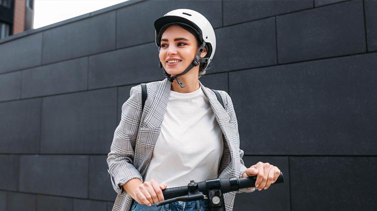 A woman wearing a helmet riding a scooter from an electric scooter rental.