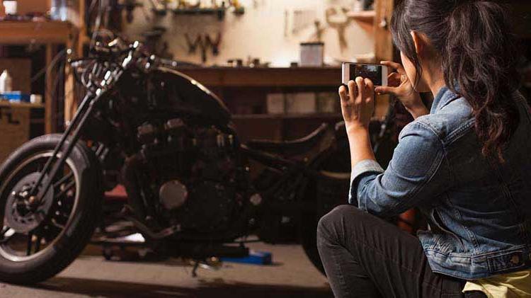 Woman taking a photo of her motorcycle with her phone.