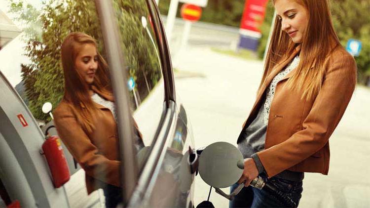 Young woman standing outside putting gas in her car.