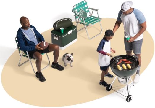 View from above of a father and son grilling hotdogs and corn on the cob as a neighb或者一个nd his dog supervise from a nearby lawn chair.